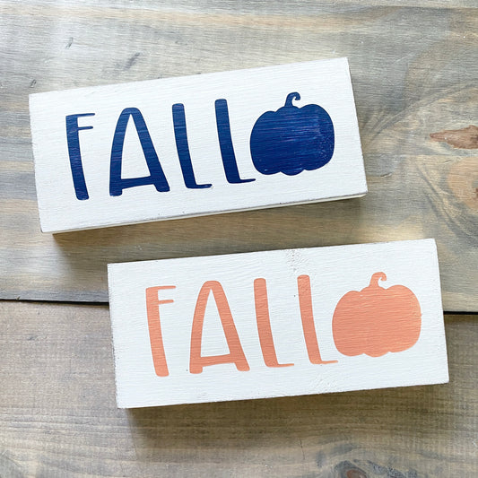 Two wooden signs with 'FALL' and pumpkin illustrations on a wooden surface