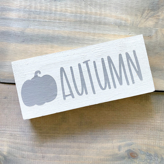 Wooden sign with 'AUTUMN' and pumpkin silhouette on a wooden surface