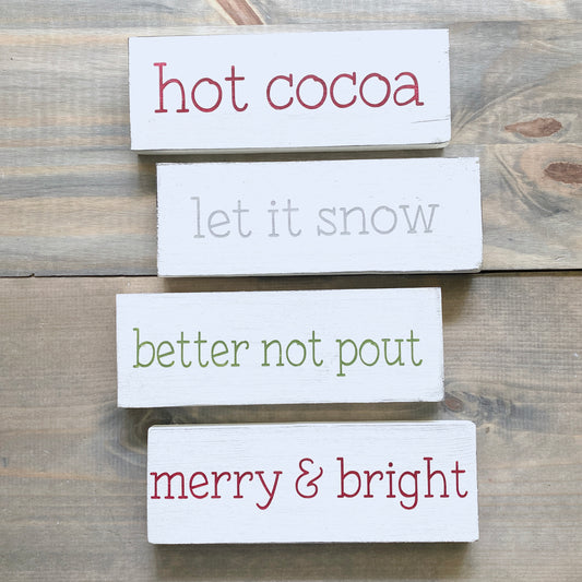 Set of wooden signs with Christmas-themed text on a wooden surface