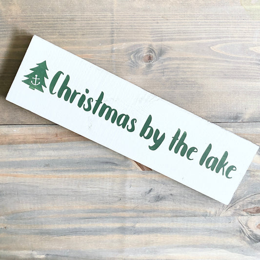 Wooden sign with 'Christmas by the lake' text and tree design on a wooden surface
