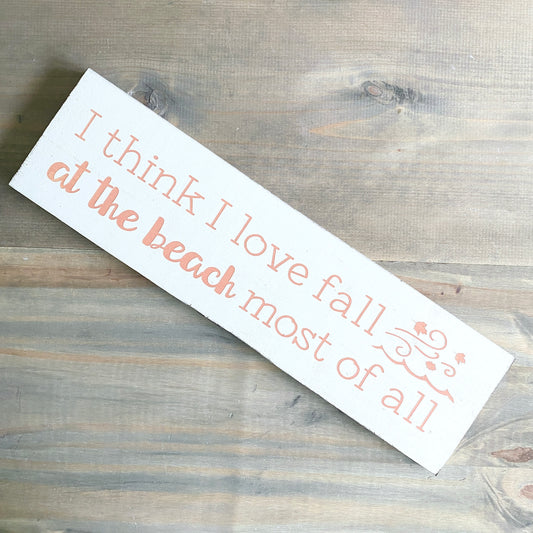Wooden sign with text 'I think I love fall at the beach most of all' on a wooden surface