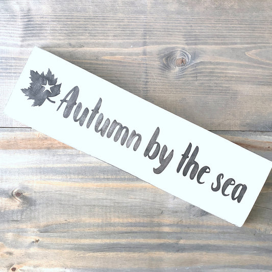wood sign with "autumn by the sea" and the silhouette of a leaf