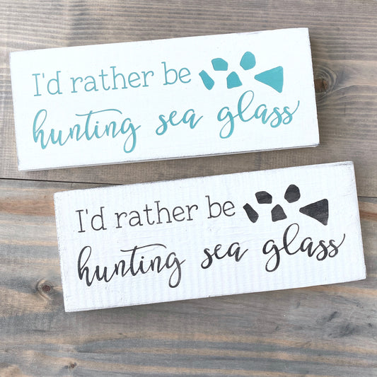 Two wooden signs with text 'I'd rather be hunting sea glass' on a wooden surface.