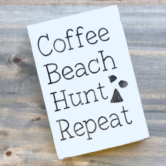 Wooden sign with 'Coffee Beach Hunt Repeat' text on a wooden surface