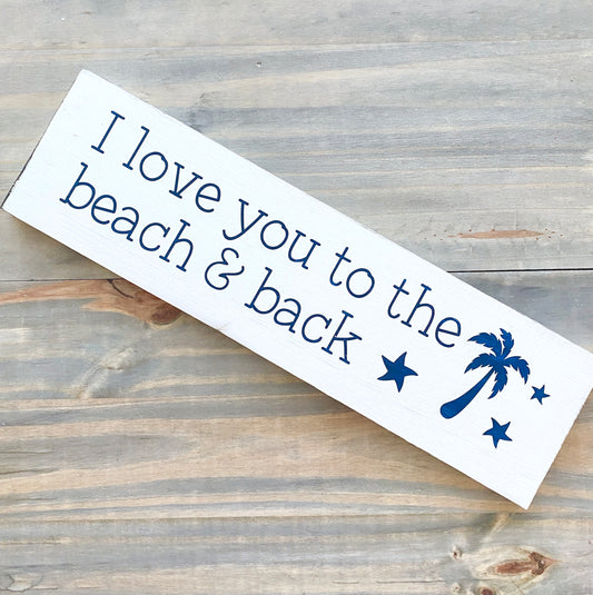 Wooden sign with 'I love you to the beach & back' text and palm tree design on a wooden surface.
