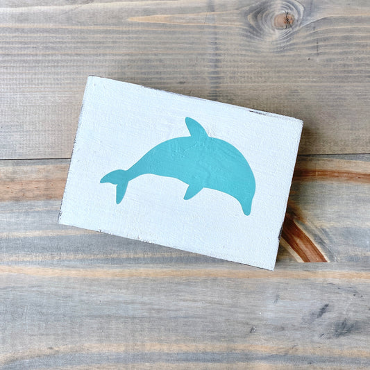 White sign with a blue dolphin design on a wooden surface
