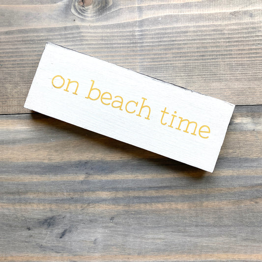 White sign with 'on beach time' text on a wooden surface
