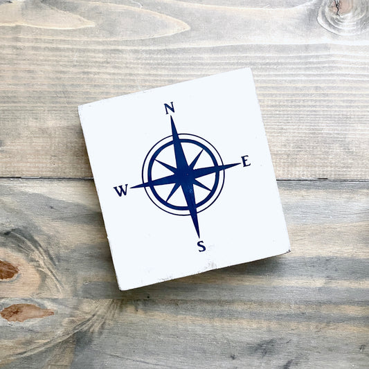 White square sign with a blue compass design on a wooden surface
