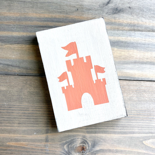 White sign with pale orange sandcastle design placed on a rustic wooden surface