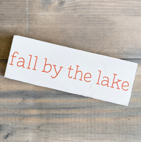 Wooden sign with 'fall by the lake' text on a wooden surface