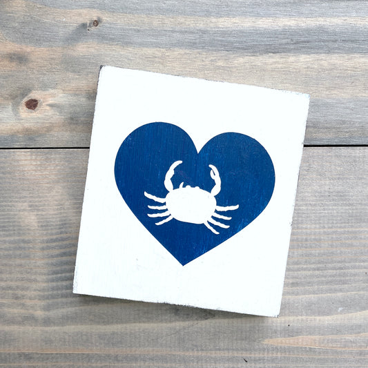 White square with a blue heart and white crab design on a wooden surface