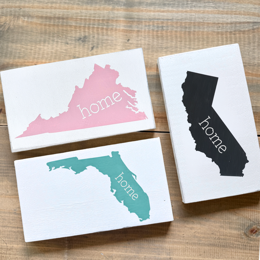 Three decorative signs with state outlines and 'home' text on a wooden surface
