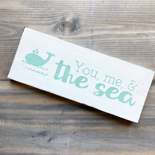 You, me, and the sea sign Coastal home decor and inspiration for the beach lover, gifts from Anchoredsouldesigns, wholesale white sign with quote and a whale in mint color displayed on a woodedn rustic surface