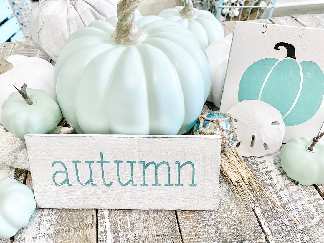 Coastal fall pumpkin display with seafoam and white HomeGoods pumpkins, a glass float, sand dollar, wheat stalks, a Pumpkin Sign, and a Custom Fall Word Sign reading autumn from Anchored Soul Designs
