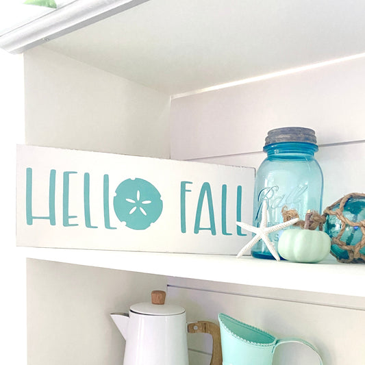 Hello Fall Sand Dollar Sign from Anchored Soul Designs styled on a white shelf with a blue Ball jar, starfish, and seafoam pumpkin, best fall decor for coastal homes