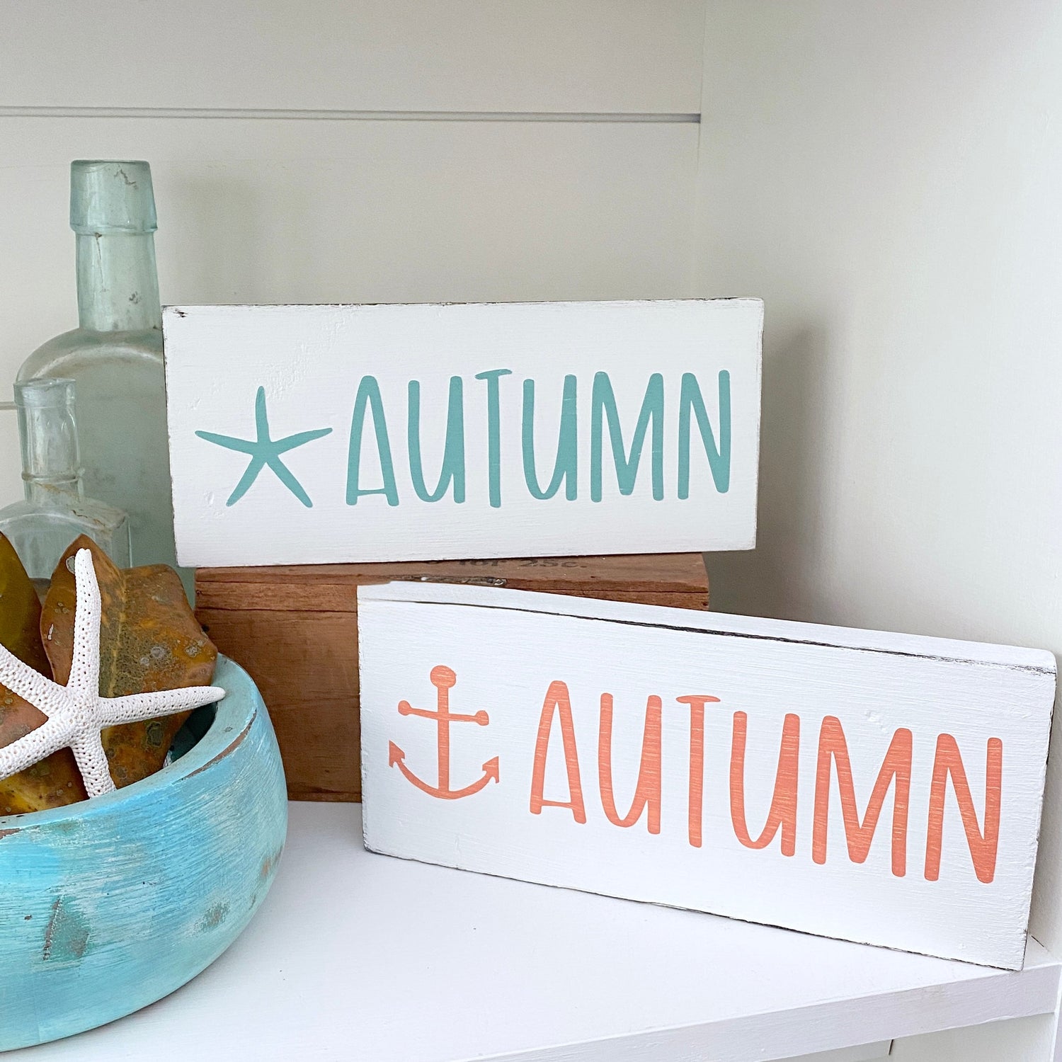 Handmade beach house fall decor featuring Starfish Autumn Sign and Anchor Autumn Sign styled on a shelf with a sea glass bottle, starfish, and coastal accents, hand-painted on real wood on Amelia Island Florida