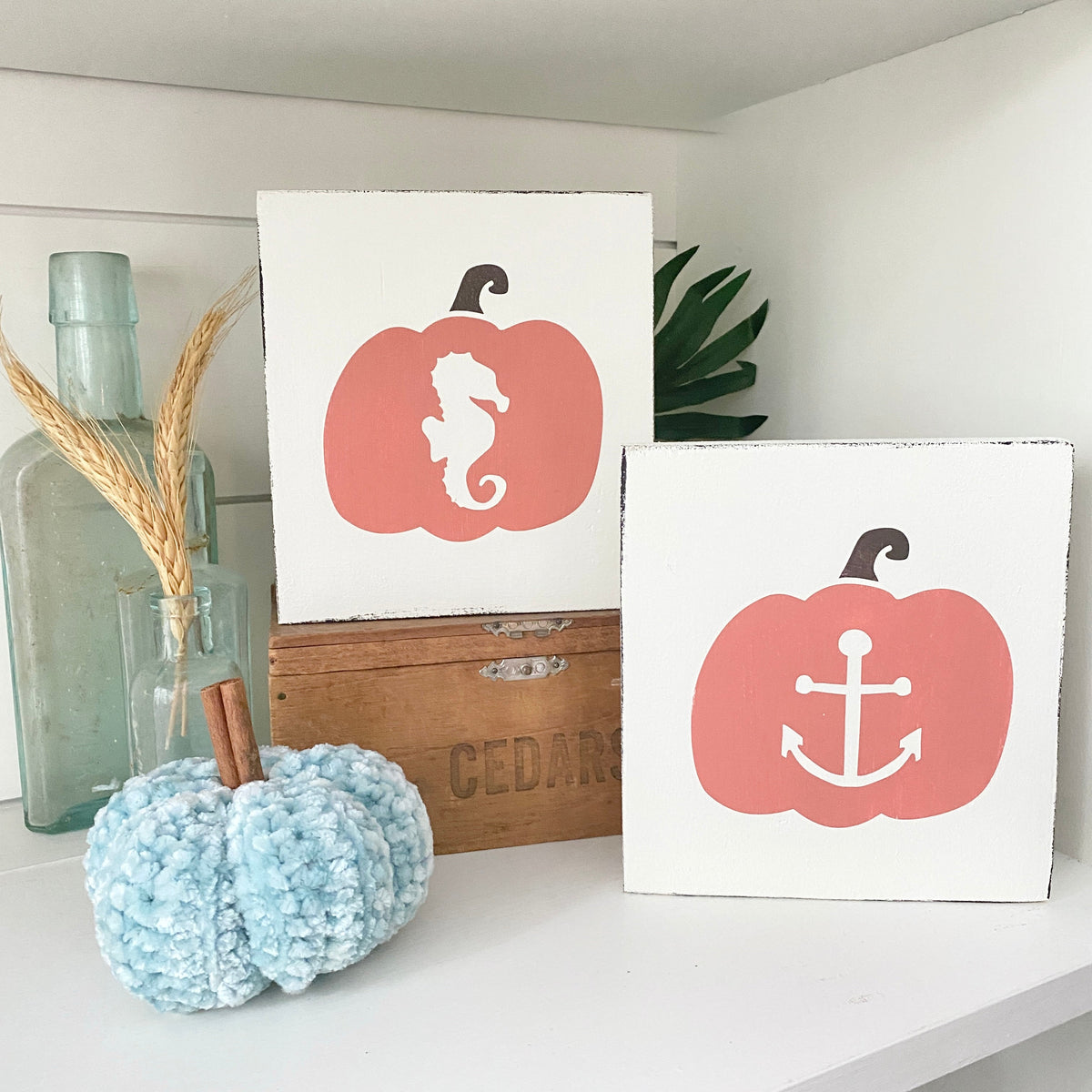 Handmade fall kitchen decor featuring a Seahorse Pumpkin Sign and Anchor Pumpkin Sign in coral and white, styled on a shelf with a sea glass bottle, dried wheat, a knit aqua pumpkin, and a vintage cedar crate
