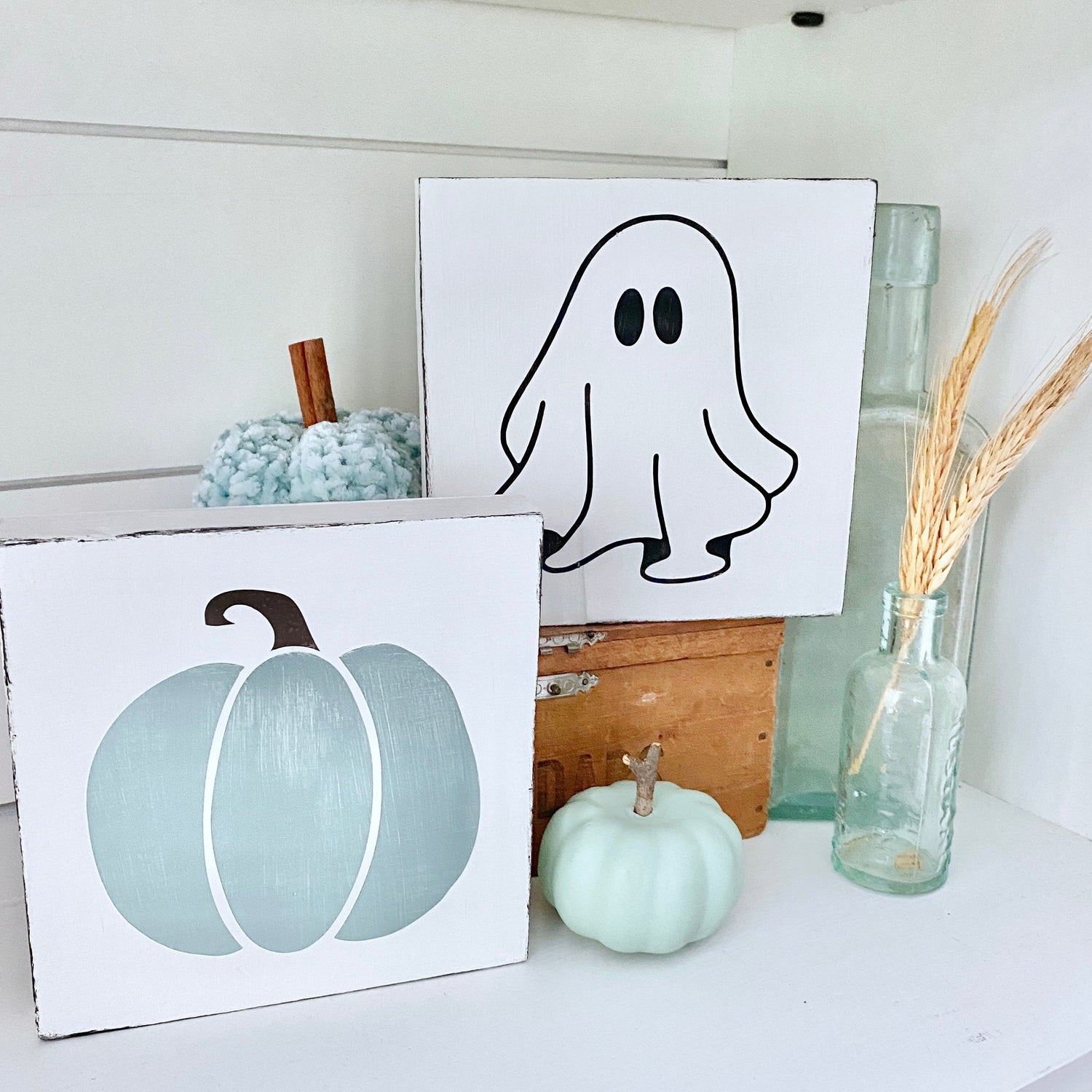 Handmade fall porch decor featuring a Coastal Pumpkin Sign and Ghost Sign in soft blue-gray and white, styled on a shelf with an aqua pumpkin, sea glass bottle, dried wheat, and a vintage wood crate, hand-painted on real wood on Amelia Island Florida