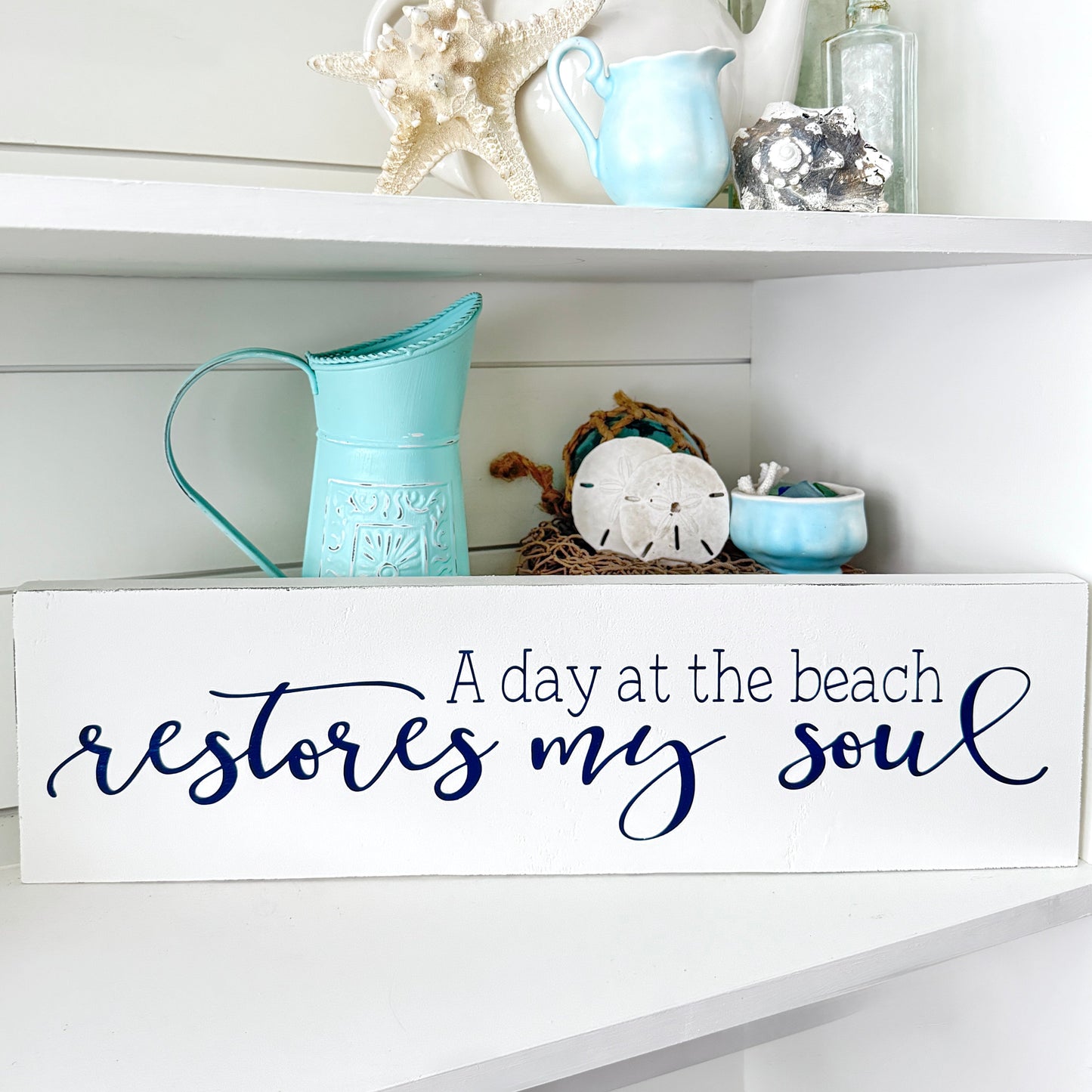 Decorative shelf with beach-themed items and a sign reading 'A day at the beach restores my soul'. coastal wood decor
