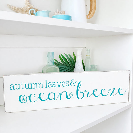 Decorative sign with 'autumn leaves & ocean breeze' text on a white shelf.