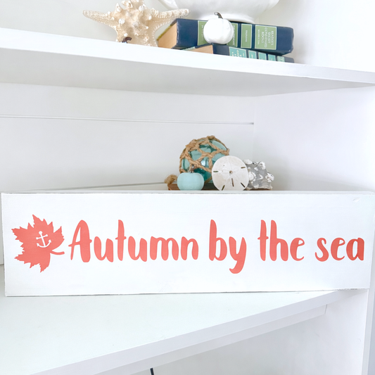 Decorative sign with 'Autumn by the sea' text on a shelf with decorative items.