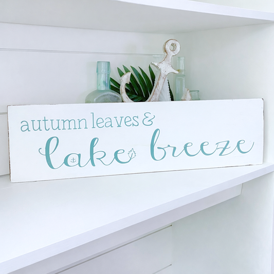 Decorative sign with 'autumn leaves & lake breeze' text on a white shelf.