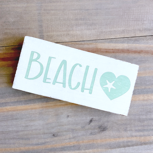 Decal with 'BEACH' text and heart design on a wooden surface