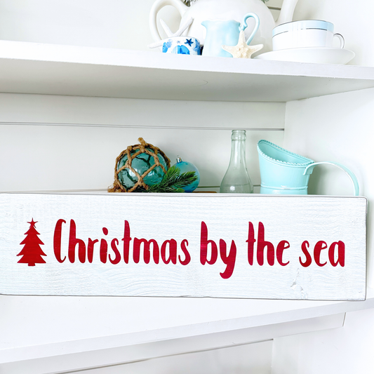 Decorative sign with 'Christmas by the sea' text on a white shelf with decorative items.
