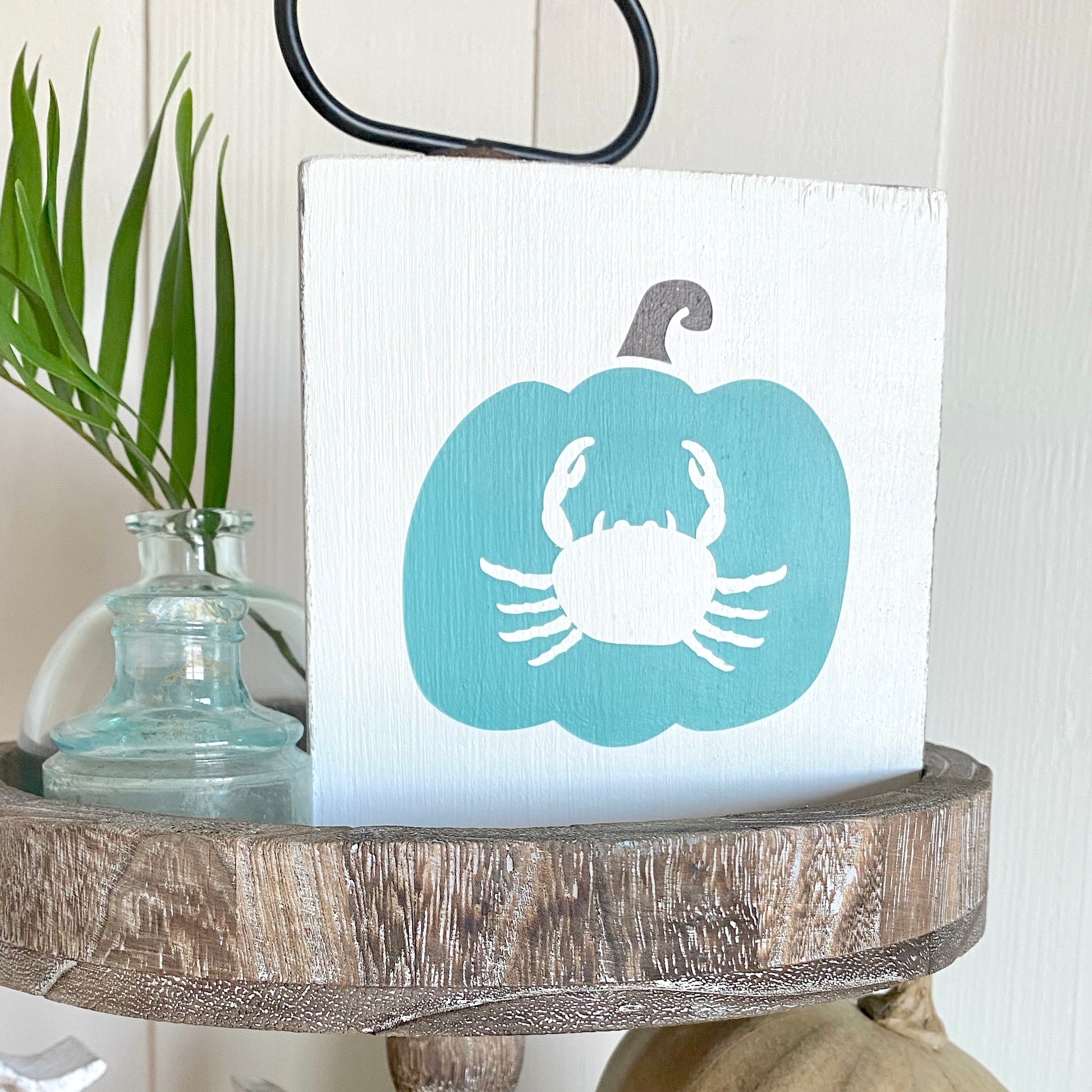 Decorative sign with a blue pumpkin and white crab design on a wooden surface.