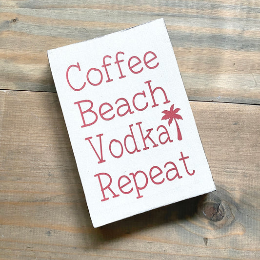 White Sign with 'Coffee Beach Vodka Repeat' text on a wooden surface
