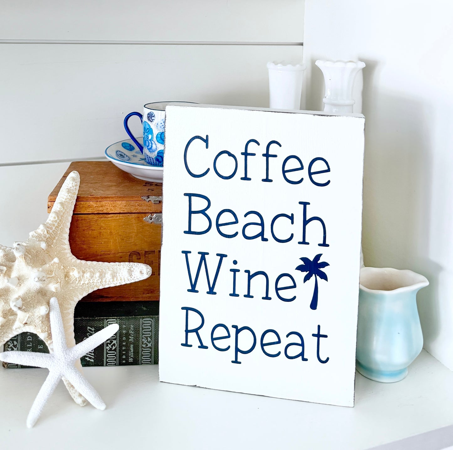 Decorative sign with 'Coffee Beach Wine Repeat' text on a shelf with starfish and mugs.