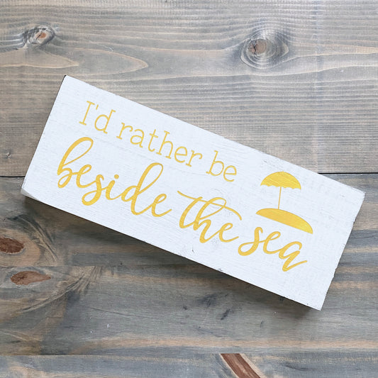 Wooden sign with 'I'd rather be beside the sea' text on a wooden surface