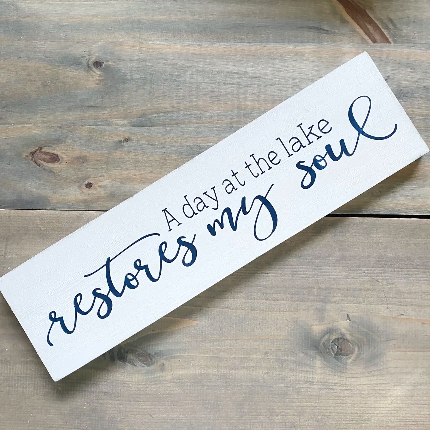 Wooden sign with text 'A day at the lake restores my soul' on a wooden surface