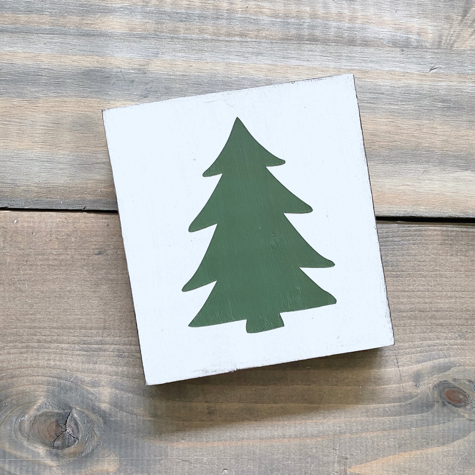 White square with a green tree silhouette on a wooden surface