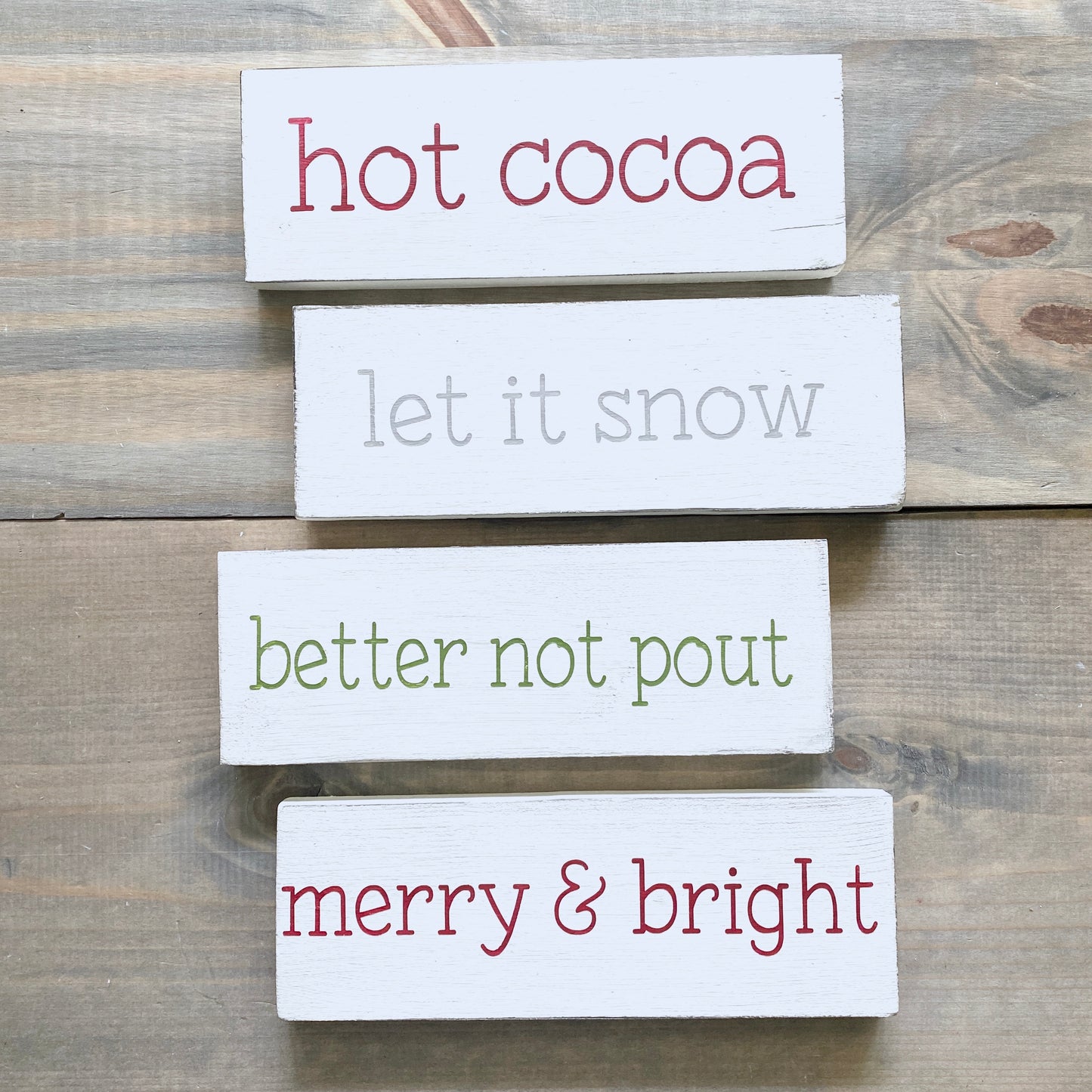 Set of wooden signs with Christmas-themed text on a wooden surface