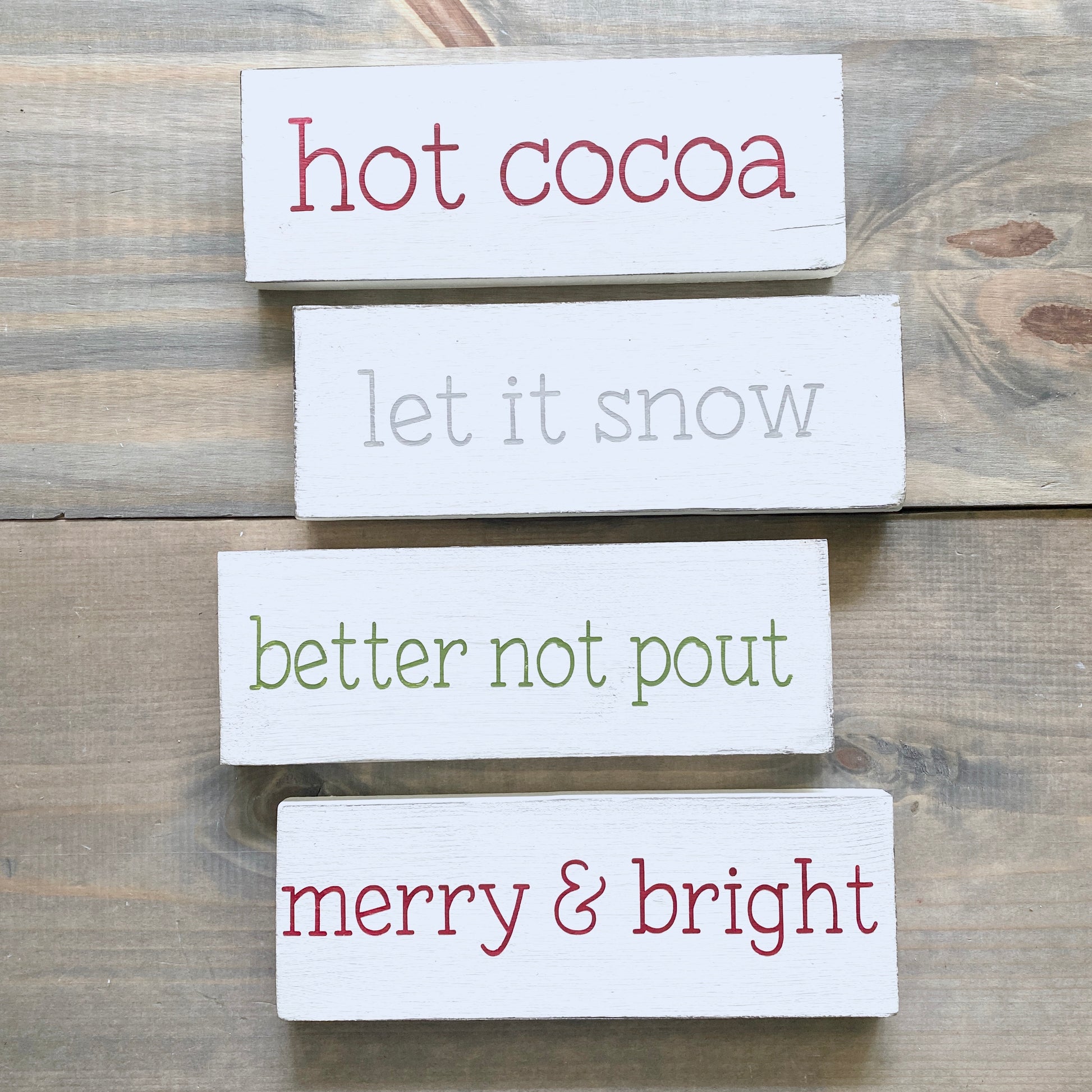 Set of wooden signs with Christmas-themed text on a wooden surface
