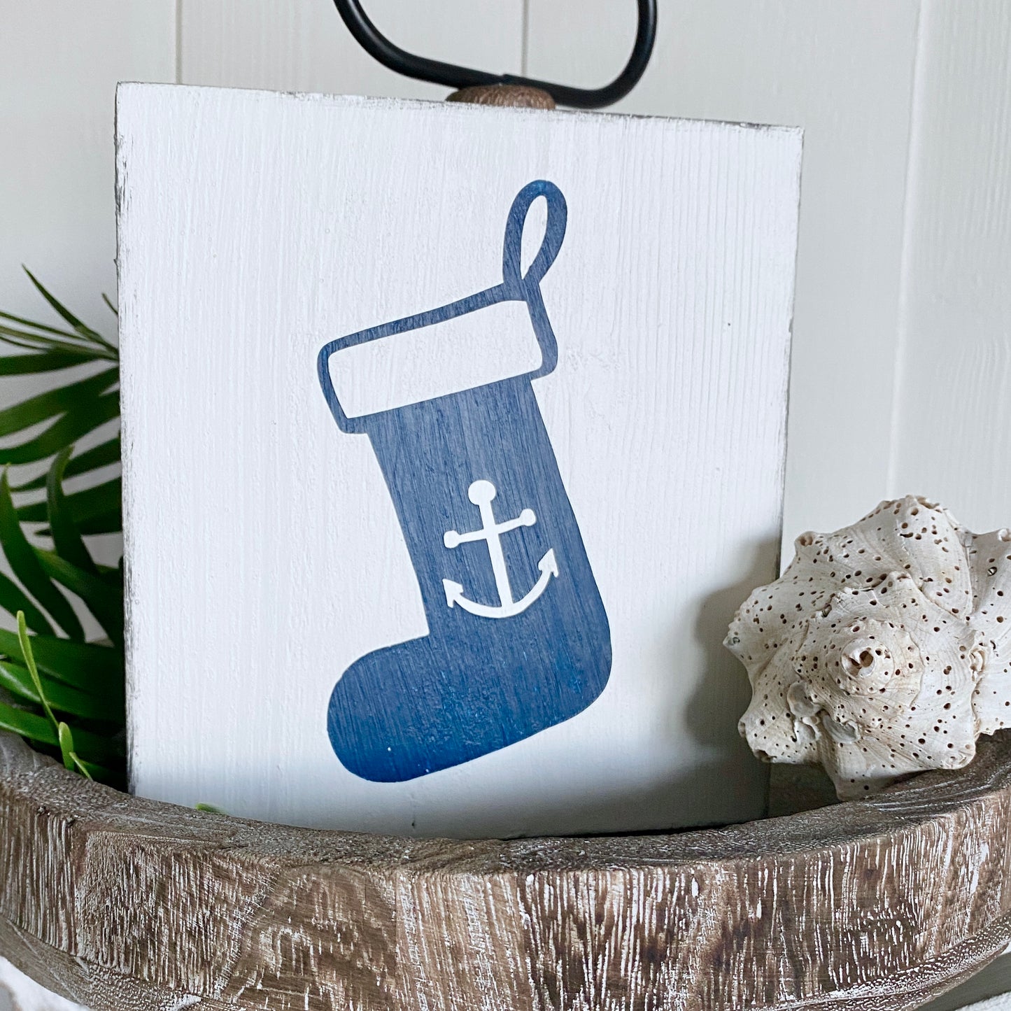 Decorative sign with a blue stocking featuring an anchor on a white background, placed in a wooden bowl.