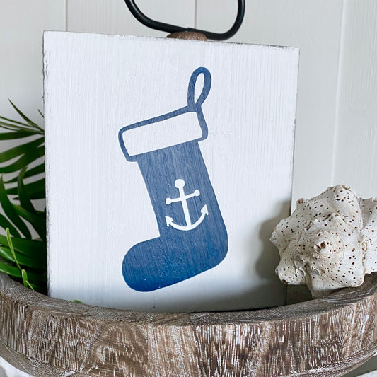 Decorative sign with a blue stocking featuring an anchor on a white background, placed in a wooden bowl.