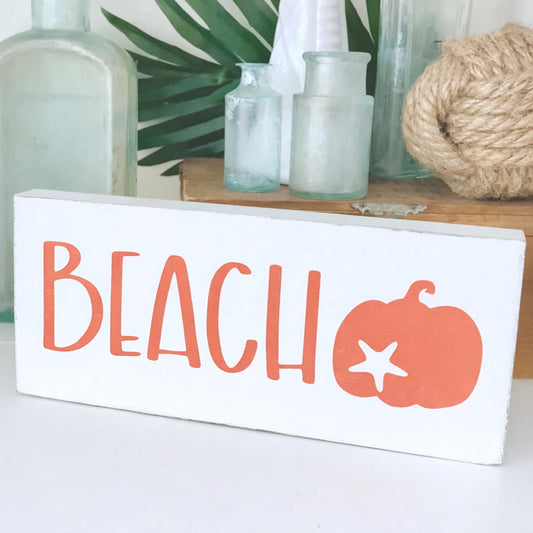 Decorative sign with 'BEACH' and pumpkin design on a white background
