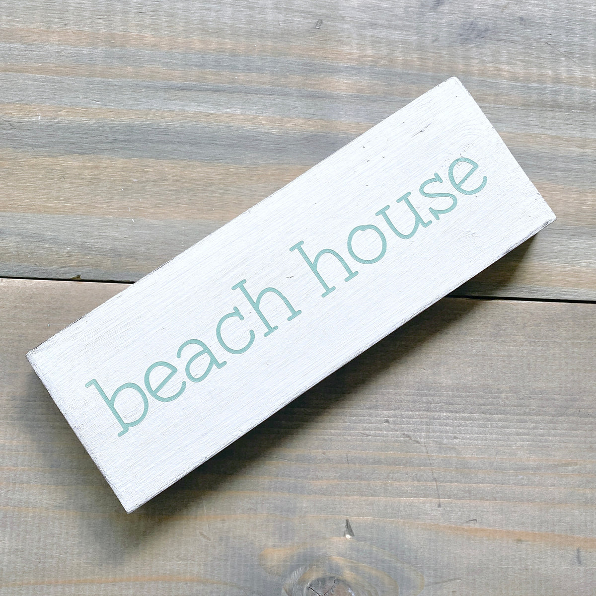 small beach house sign in mint green on a rustic wood surface
