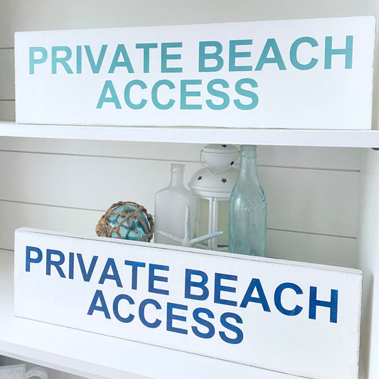 Two white wooden signs with 'PRIVATE BEACH ACCESS' text, in aqua and navy, displayed on a white shelf with decorative coastal decor