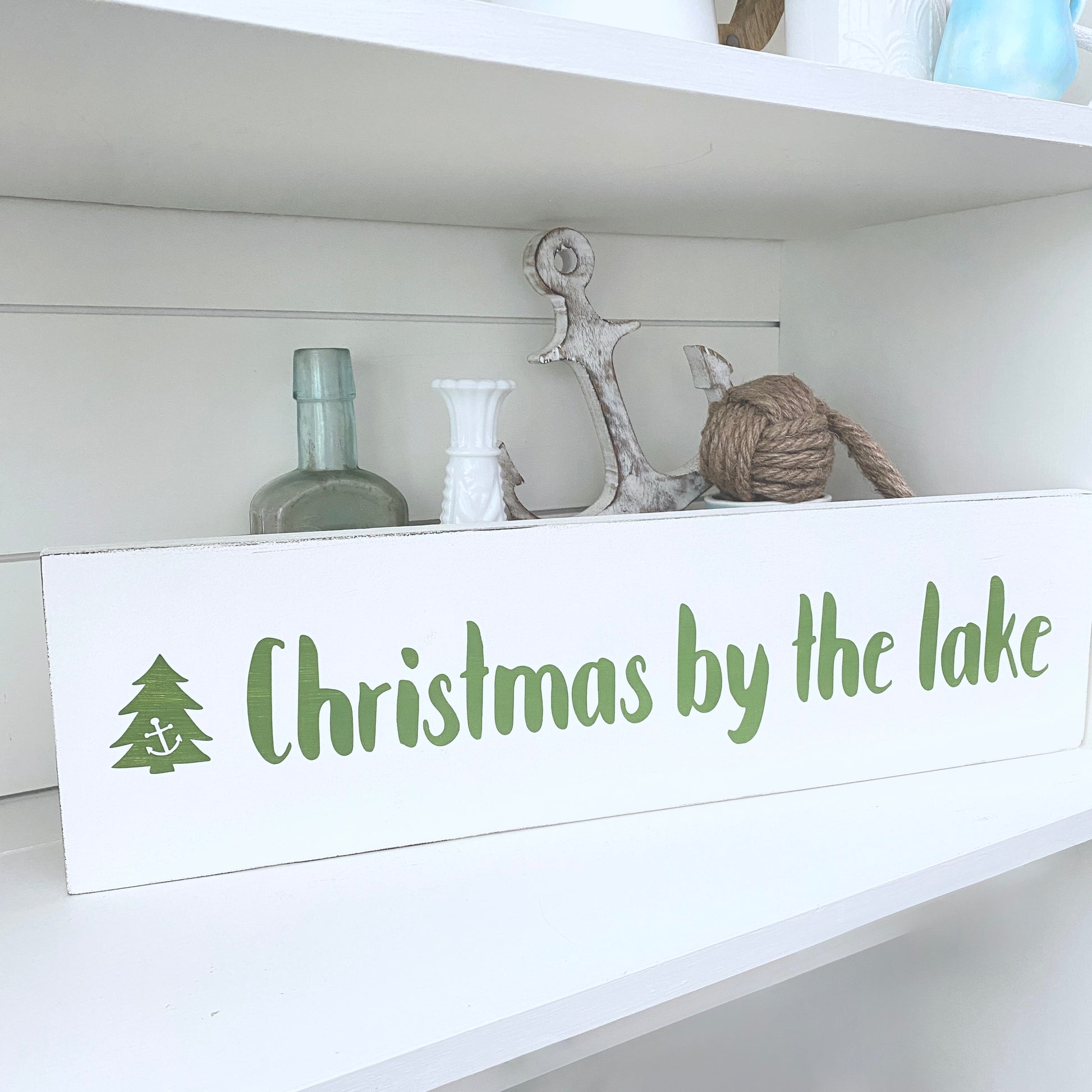 Decorative sign with 'Christmas by the lake' text on a shelf with decorative items.