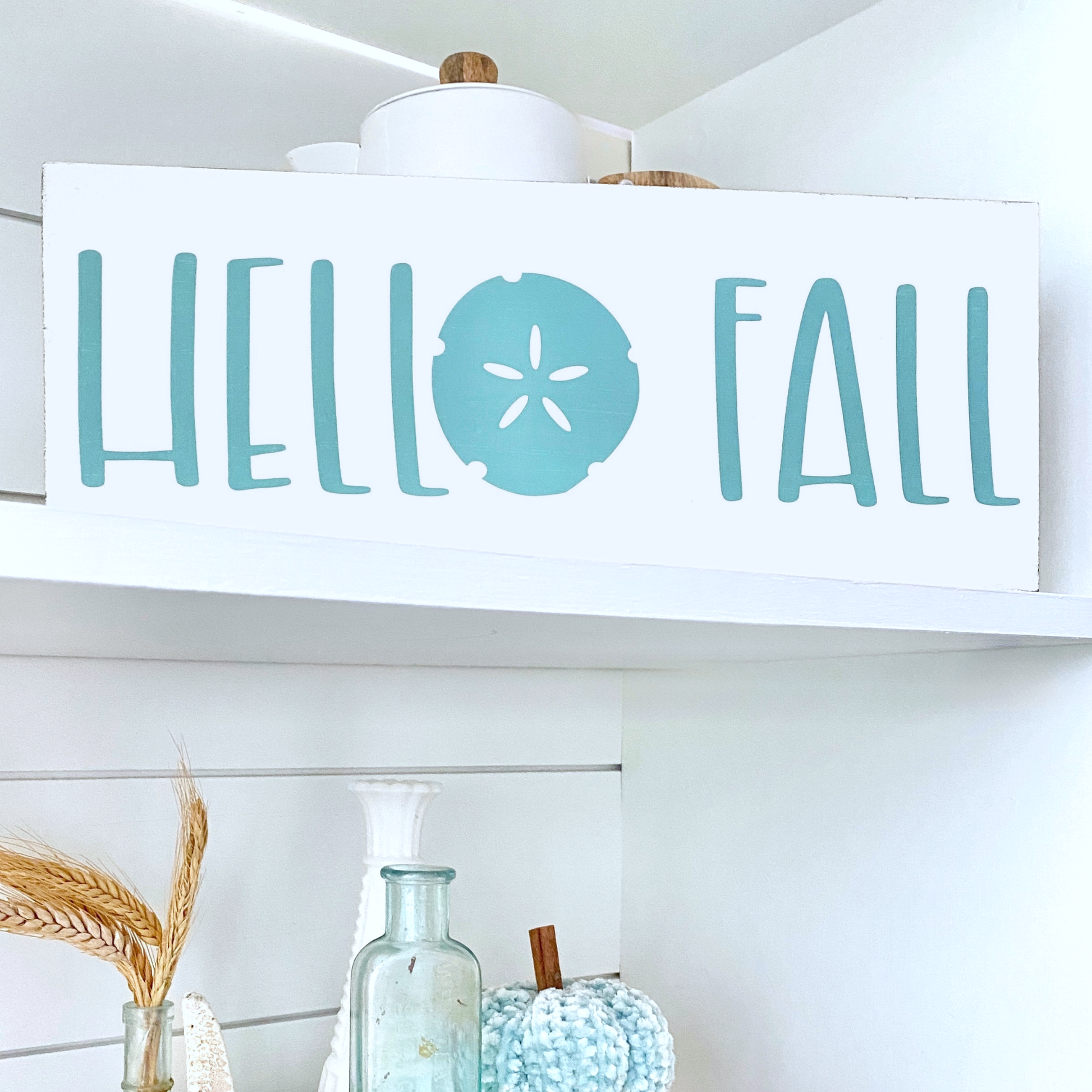Decorative sign with 'Hello Fall' text on a shelf with decorative items.