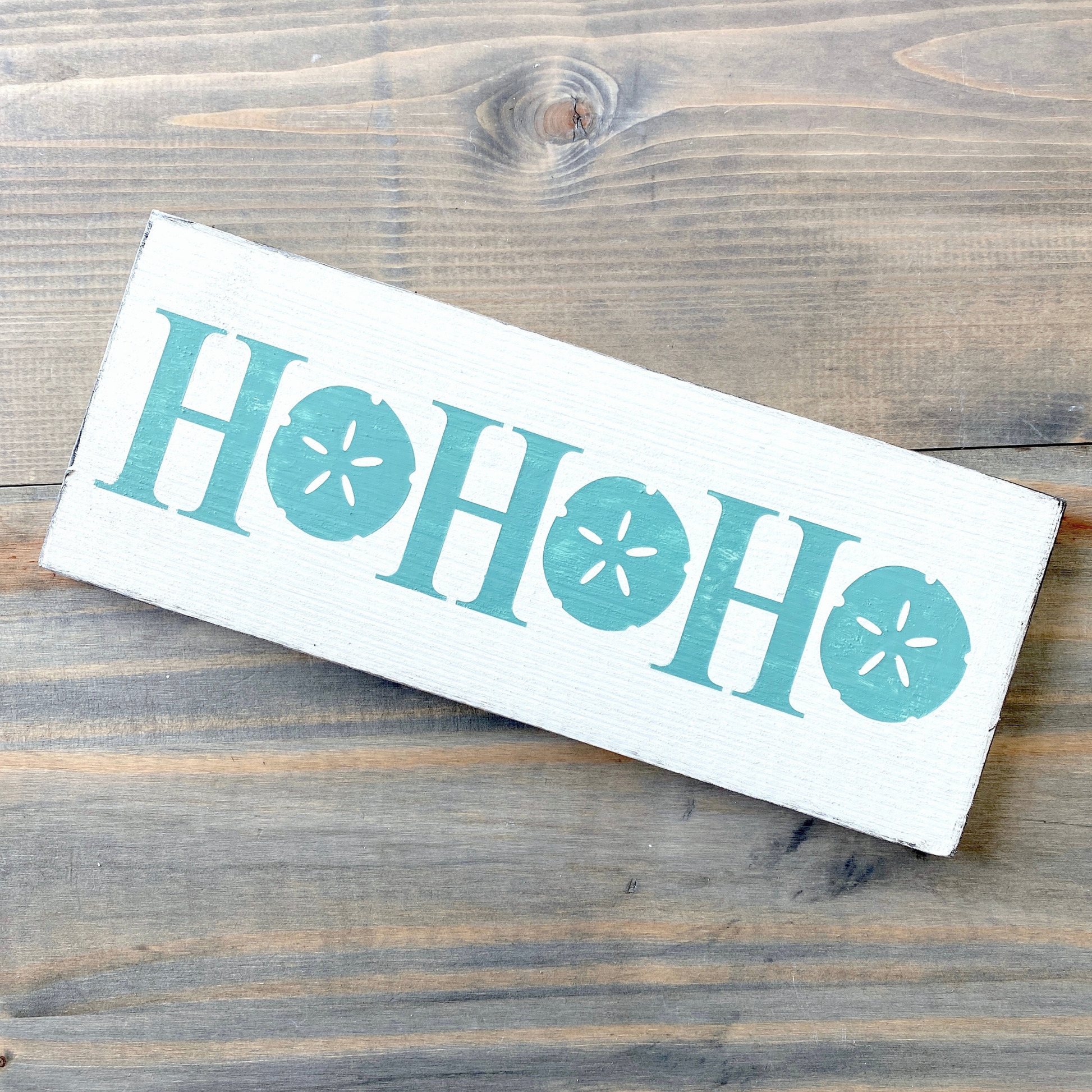 Wooden sign with 'HO HO HO' text  with sand dollars on a wooden surface