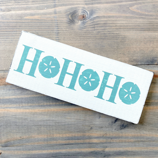 Wooden sign with 'HO HO HO' text  with sand dollars on a wooden surface