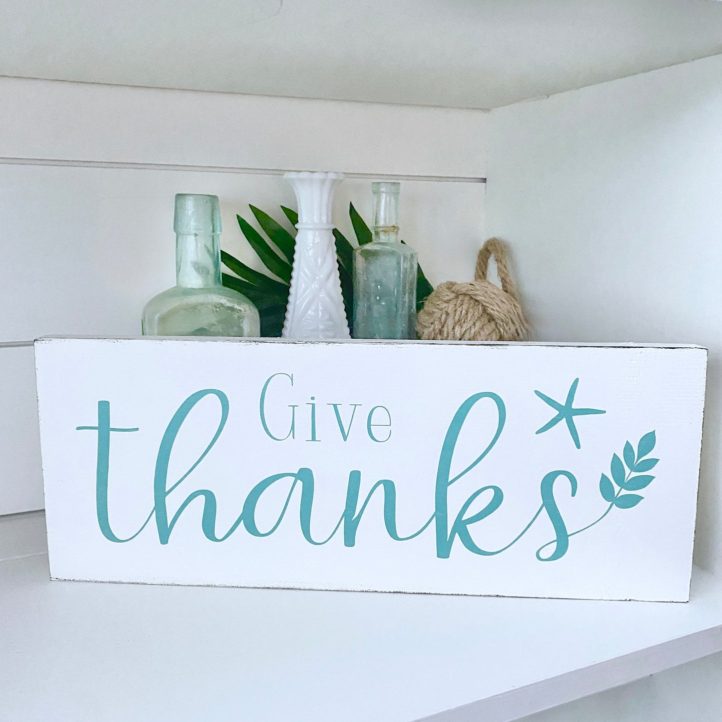 Wooden sign with 'Give thanks' text on a shelf with decorative items.