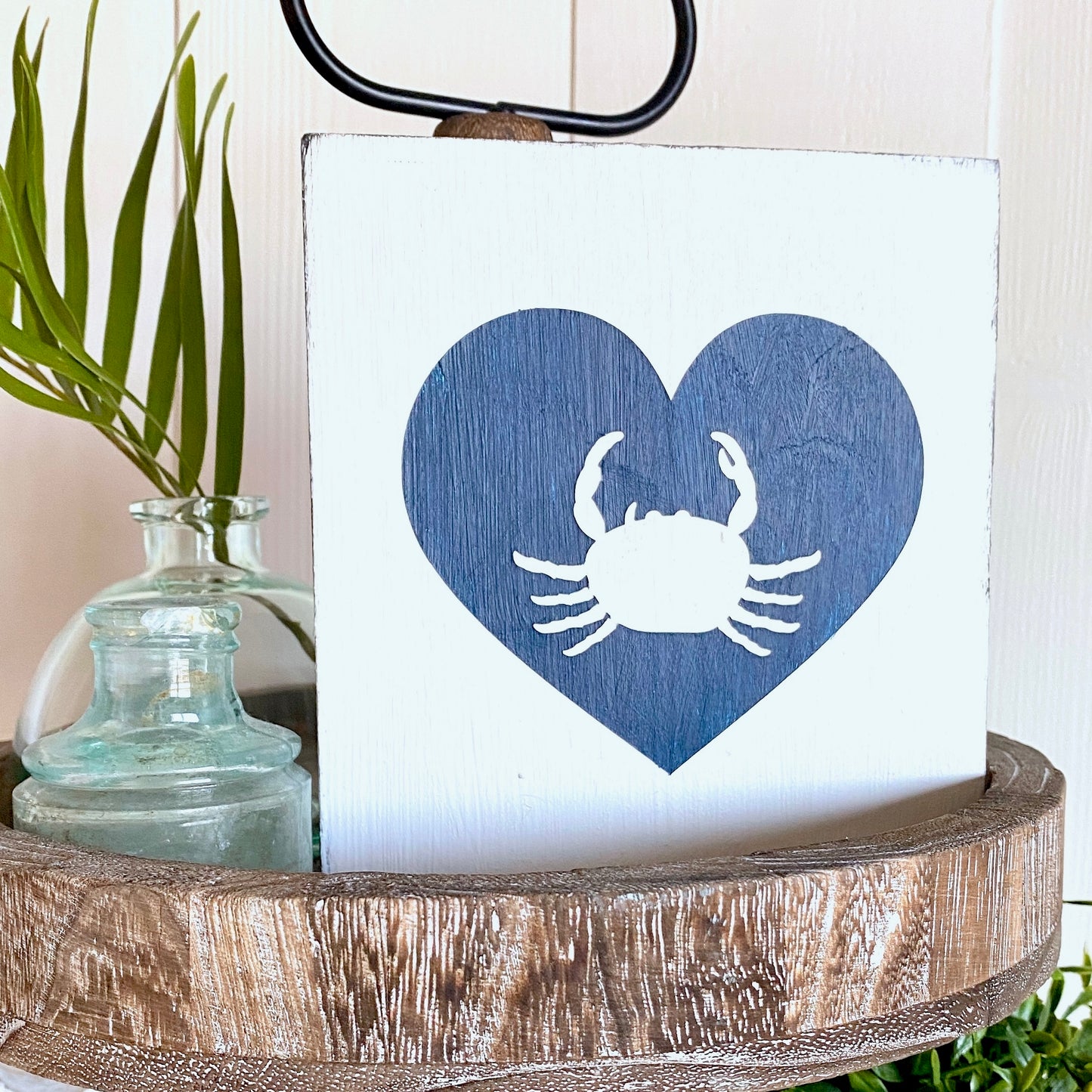 Decorative sign with blue heart and white crab design on a wooden surface.