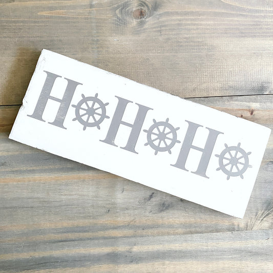 White rectangular stencil with 'HOHOHO' text and ship wheel designs on a wooden surface