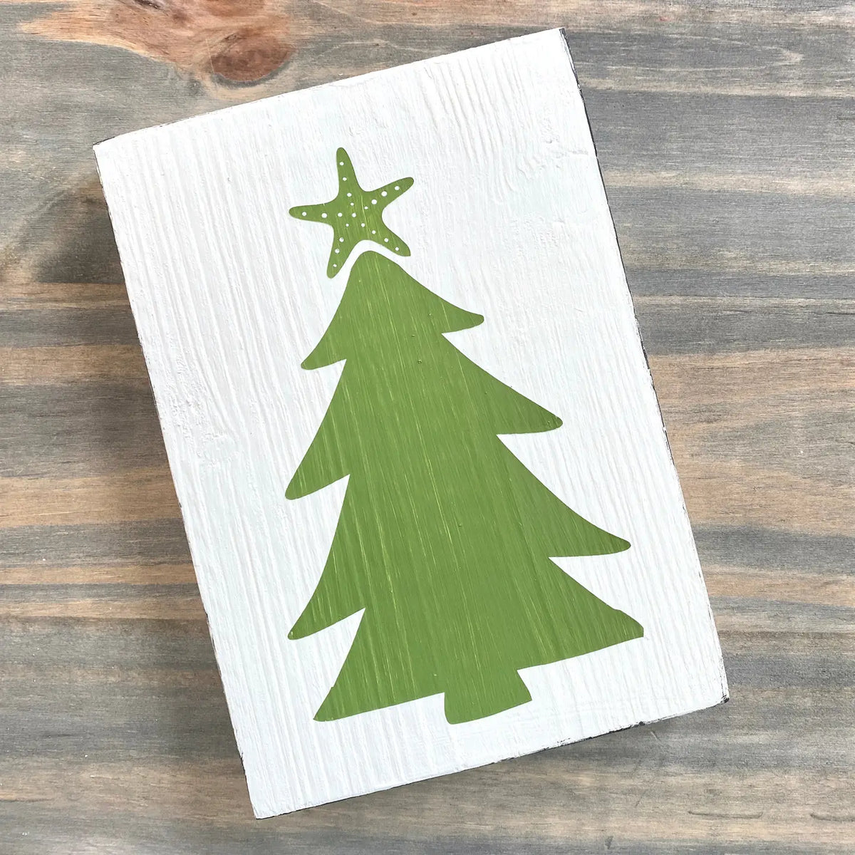white coastal christmas sign with a green christmas tree and starfish topper, placed on a wooden background