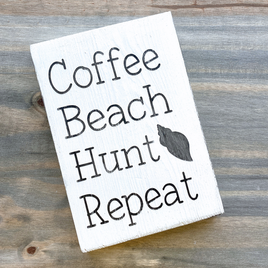 Wooden sign with 'Coffee Beach Hunt Repeat' text on a wooden surface